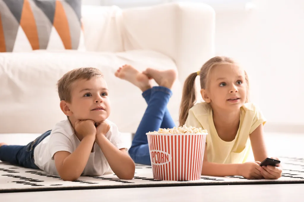 Children laying on a carpet eating popcorn