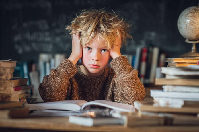 Un niño con cara de agobio rodeado de libros